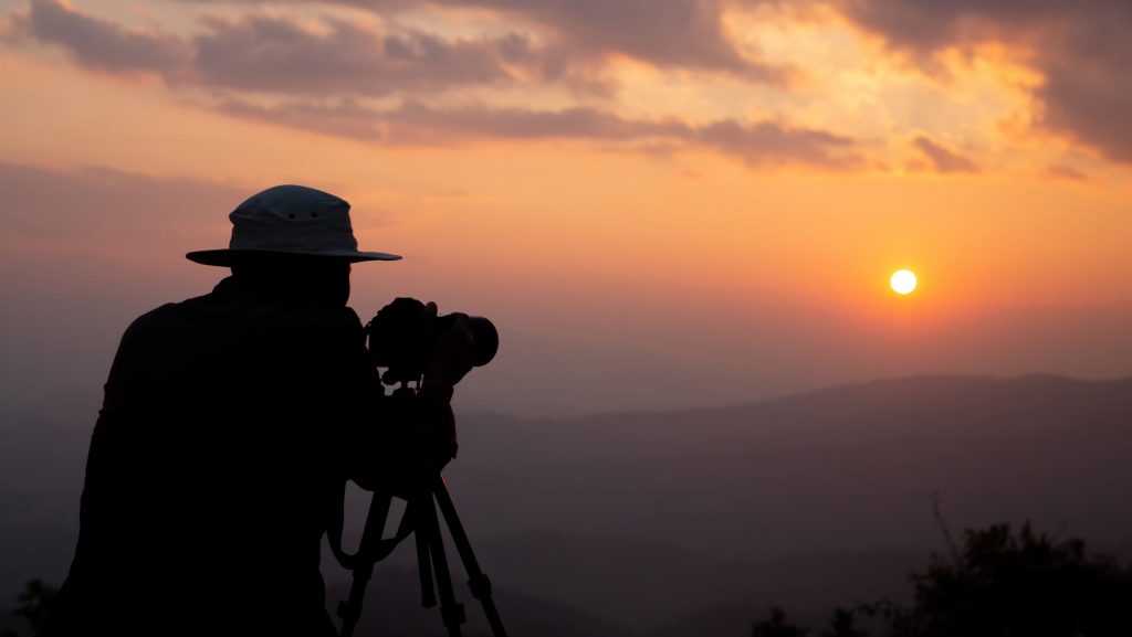 silhouette of a photographer who shoots a sunset in the mountain